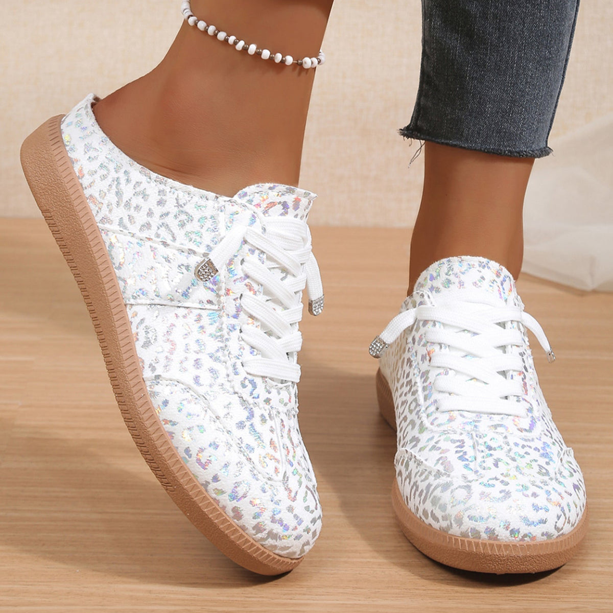 White floral sneakers with brown soles worn with blue jeans on a wooden floor.